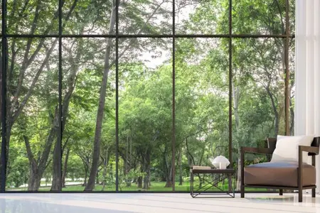 Moderní interiér s křeslem u velkých prosklených oken s výhledem do zeleného lesa.