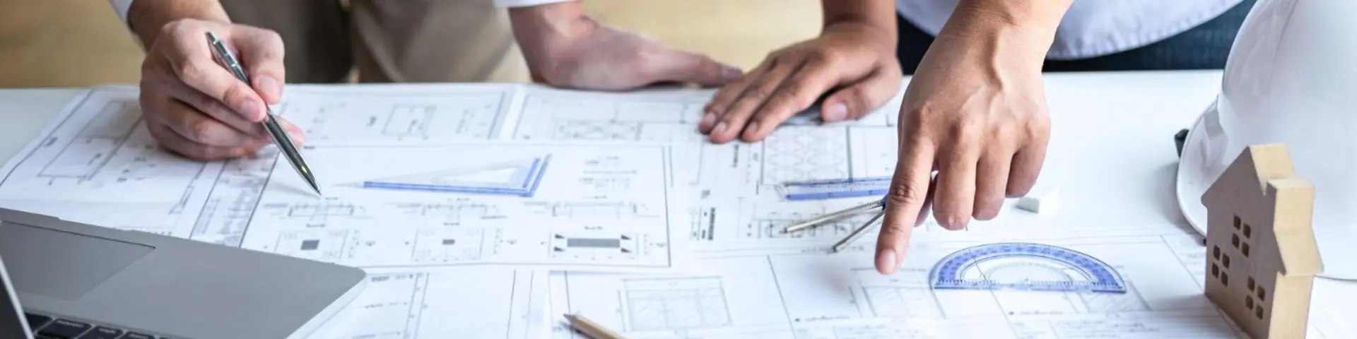 Dva lidé konzultují technické výkresy na stole a ukazují na detaily stavebních plánů