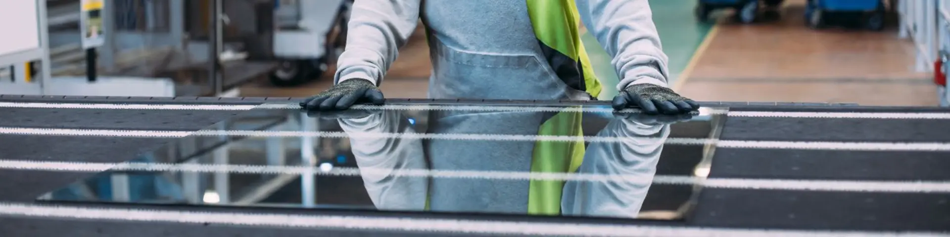 Detail pracovníka ve výrobě Glassolutions, který v rukavicích manipuluje s velkou tabulí stavebního skla na pracovním stole.