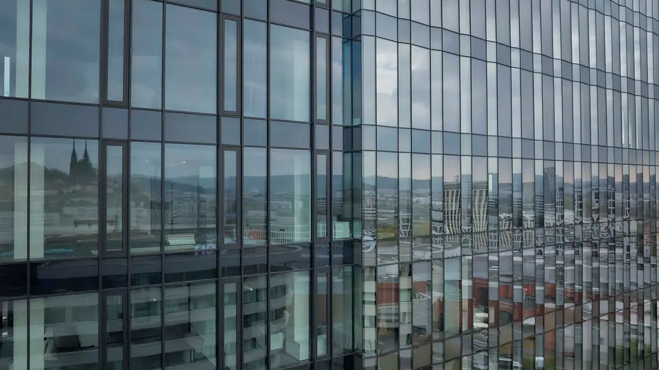 Detail prosklené fasády budovy s odrazem městské zástavby a panoramatu.