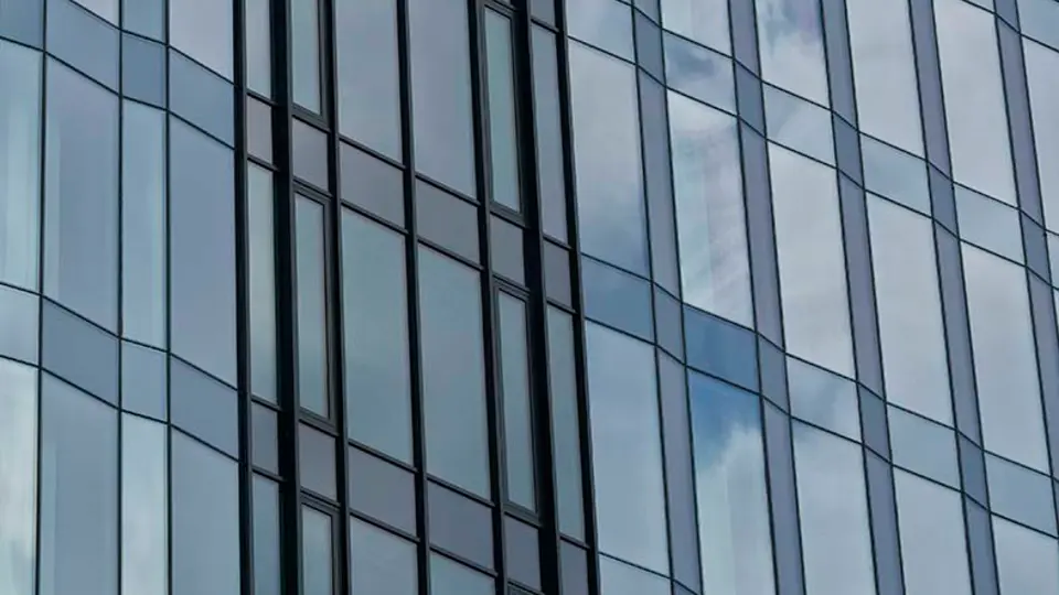Detail vertikálně členěné prosklené fasády budovy s odrazem oblohy v jednotlivých panelech.