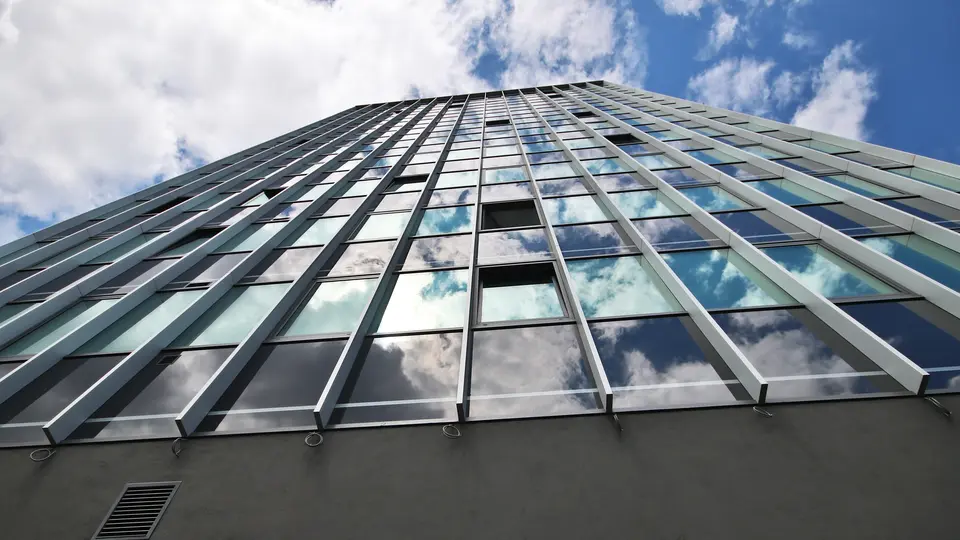 „Pohled zespodu na prosklenou fasádu budovy Černá perla v Ostravě s vertikálním členěním a odrazem oblohy v oknech.