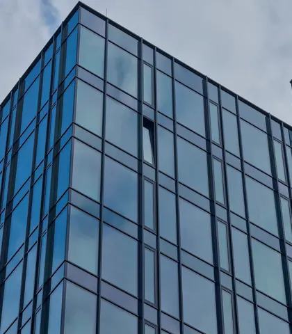 Detail prosklené fasády moderní budovy s vertikálním členěním a odrazem oblohy.